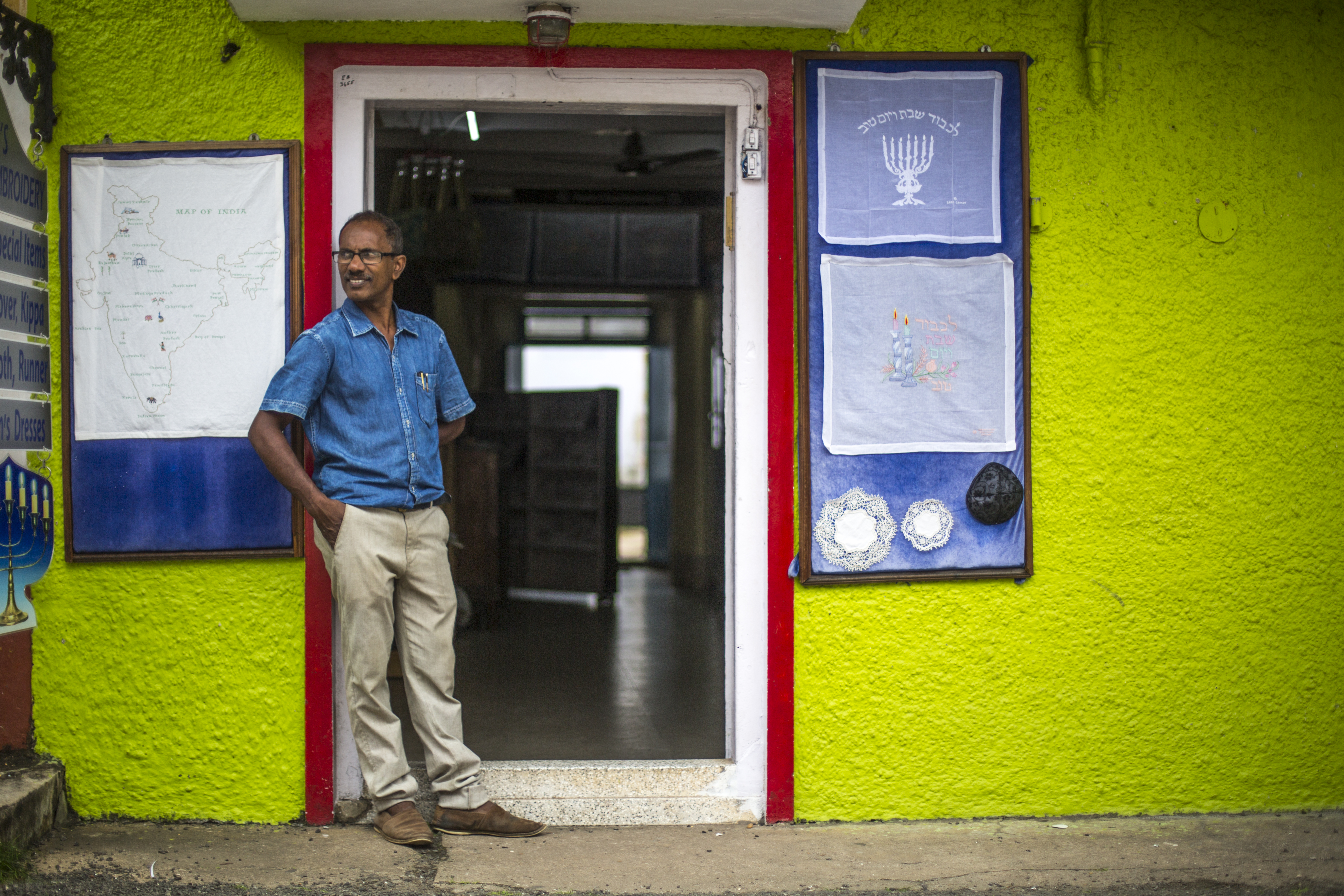 Thaha Ibrahim in the doorway of Cohen's embroidery shop. On his right is an embroidered map of India, encapsulating the unique mix of Jewish and Indian influences in the shop. A Muslim, he became interested in Judaism as a boy helping his uncle sell postcards outside of Cohen's shop. 