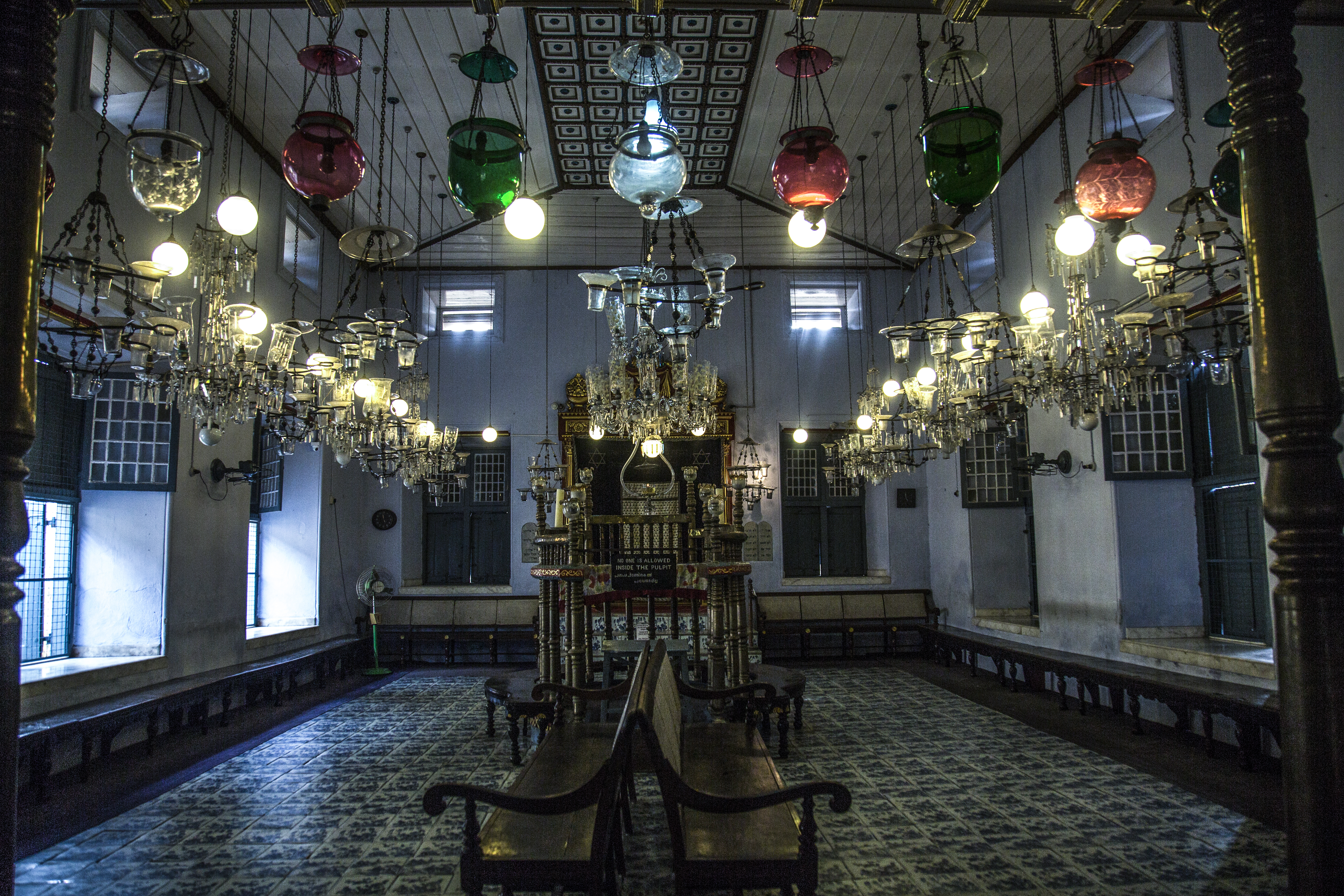 Paradesi Synagogue, quiet after a day of tourists bustling in and out. At the front of the building, a sign asks visitors to remove their shoes before entering. Entering a synagogue barefoot is not a common Jewish practice; it's adopted from Indian traditions.