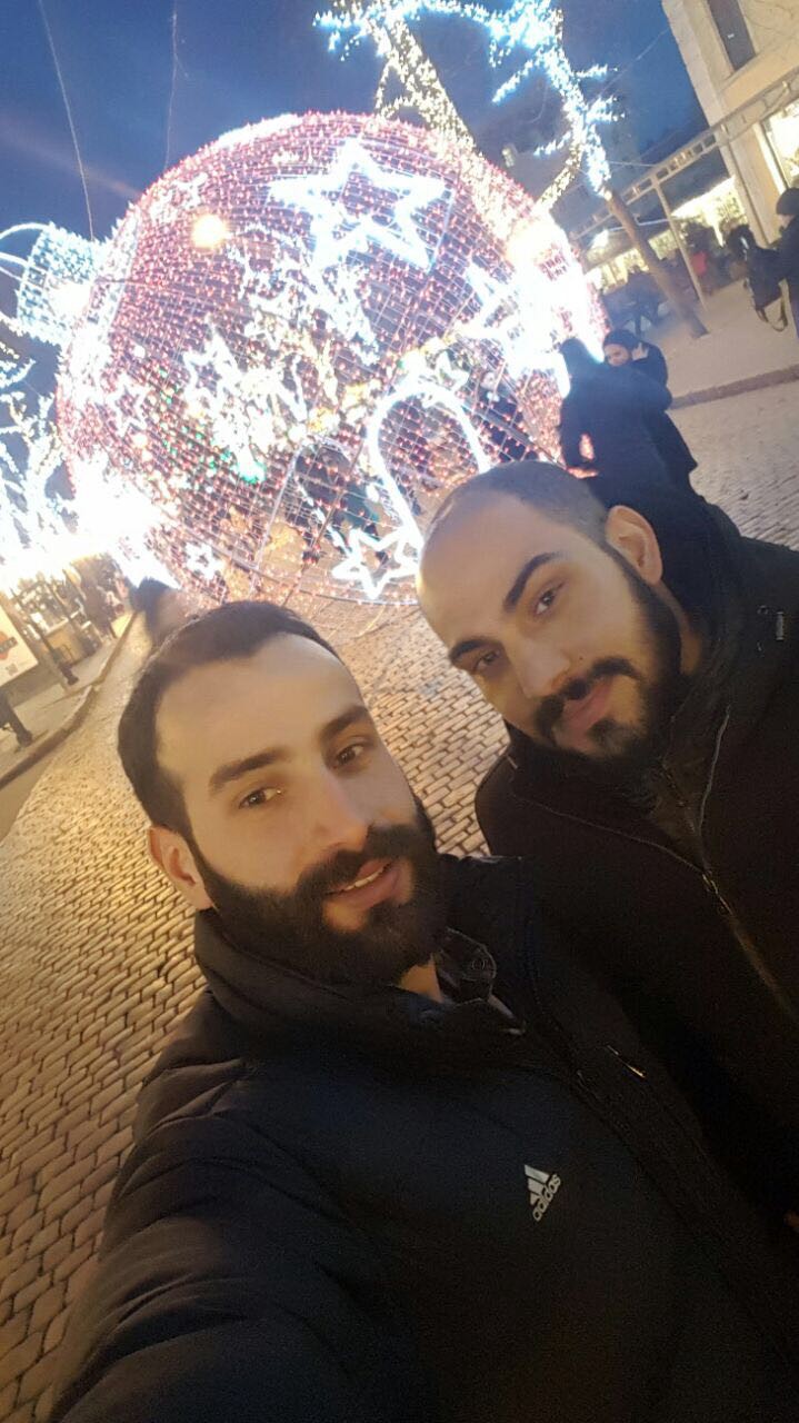 Photo showing two young men in front of a Christmas light display