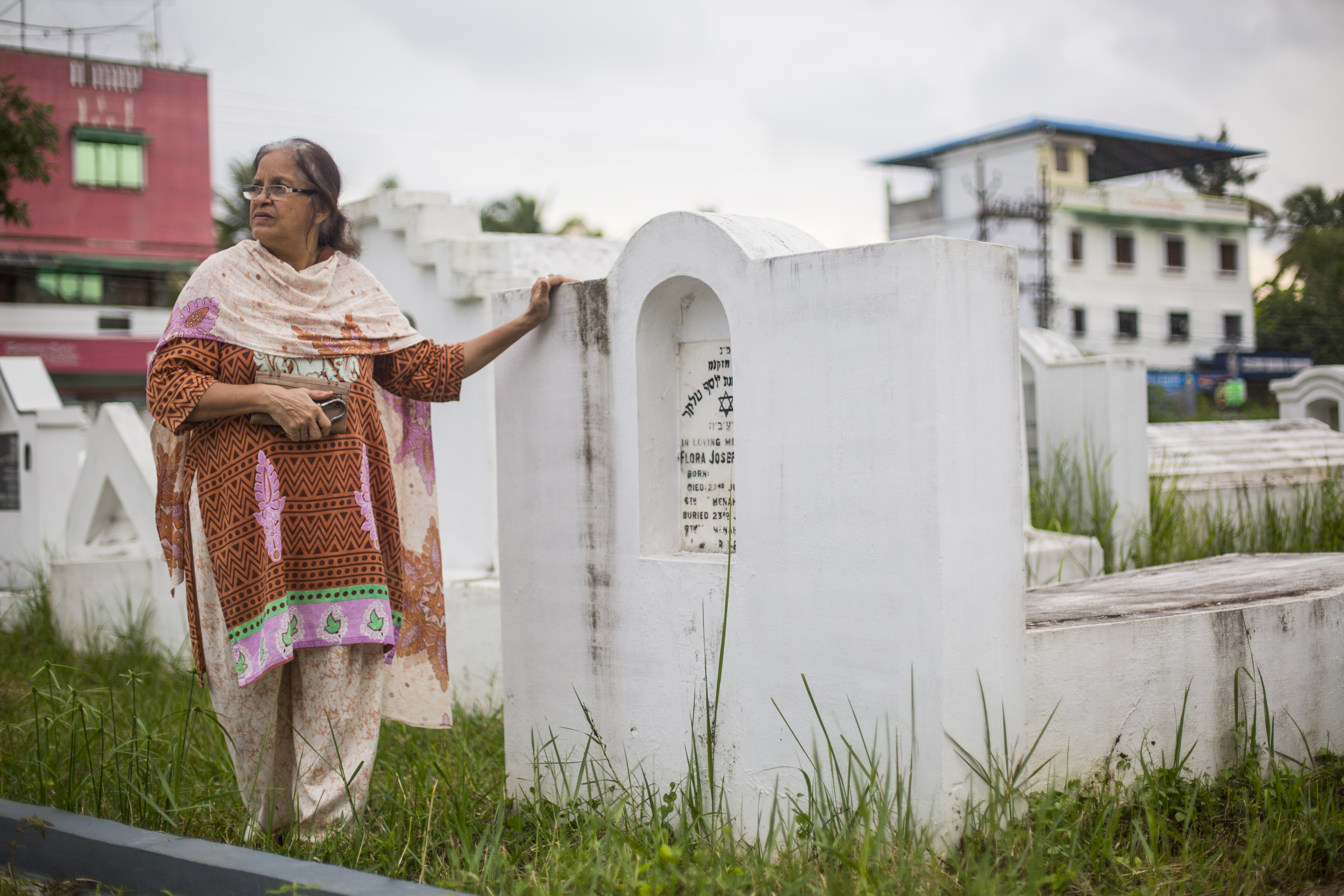 Ofera Elias, Babu's wife, stands at her grandmother's grave in the Ernakulam Jewish Cemetery. She points out the weeds growing tall around the tombstones. 