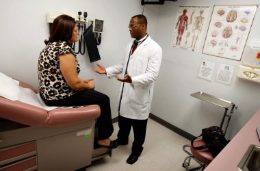 Photo showing a doctor talking to a patient sitting on a bed in an exam room