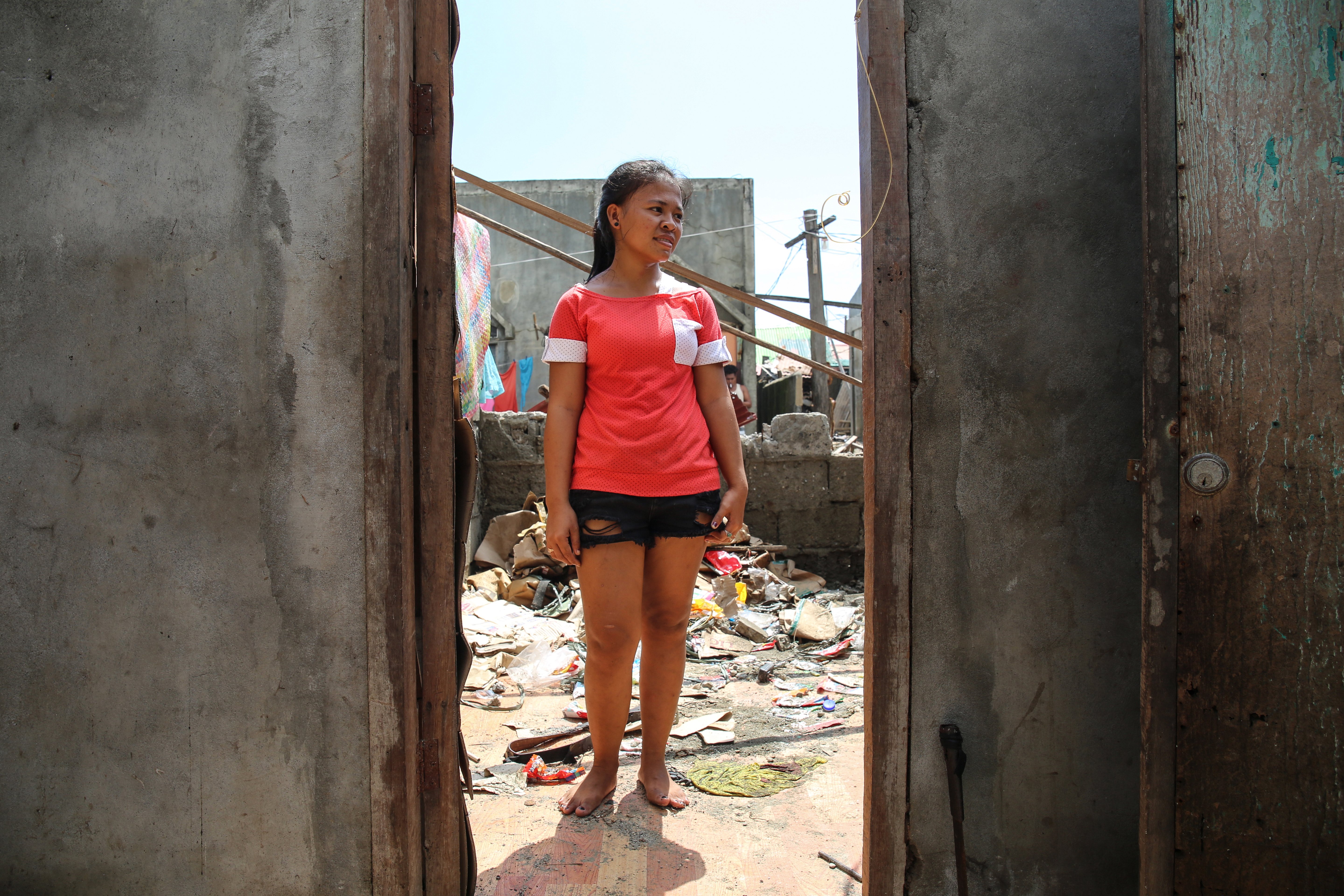 Sasana Raquini, 18, stands in her home in Aparri, which lost both its walls and roof. Today, she is cleaning up alone as her father and brother are out fishing. 