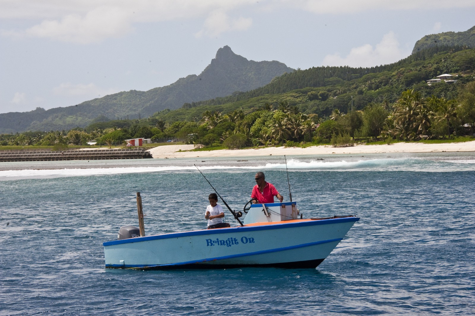 Photo showing two people fishing in a small motorboat just offshore of a tropical island