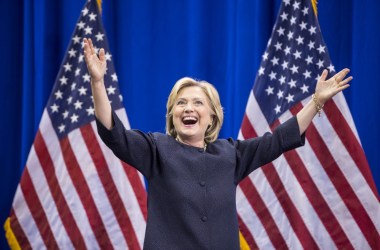 Photo of Hillary Clinton in front of American flags, with her arms upraised