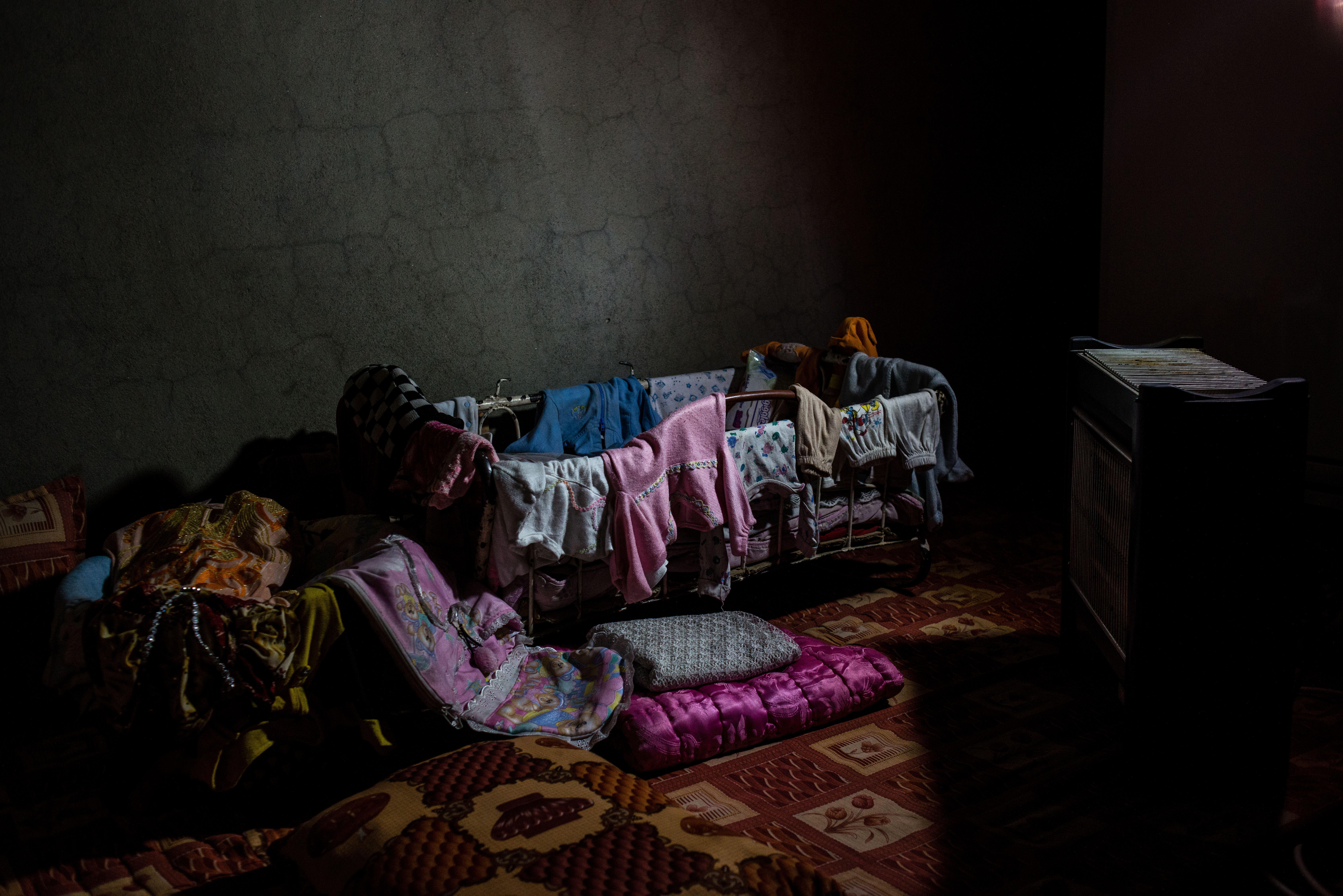 A mother holds a light to show the clothes of her granddaughter, who was killed while fleeing across the frontline—along with everyone else from her family, except for her son.