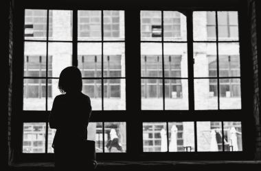 A woman in silhouette gazes out a window (and is a neutral image for stories about stuff like depression)