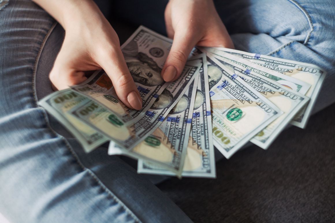 Woman holding a bunch of money in hundred dollar bills.