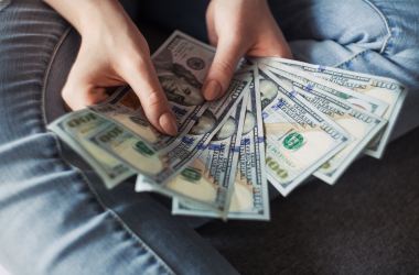 Woman holding a bunch of money in hundred dollar bills.