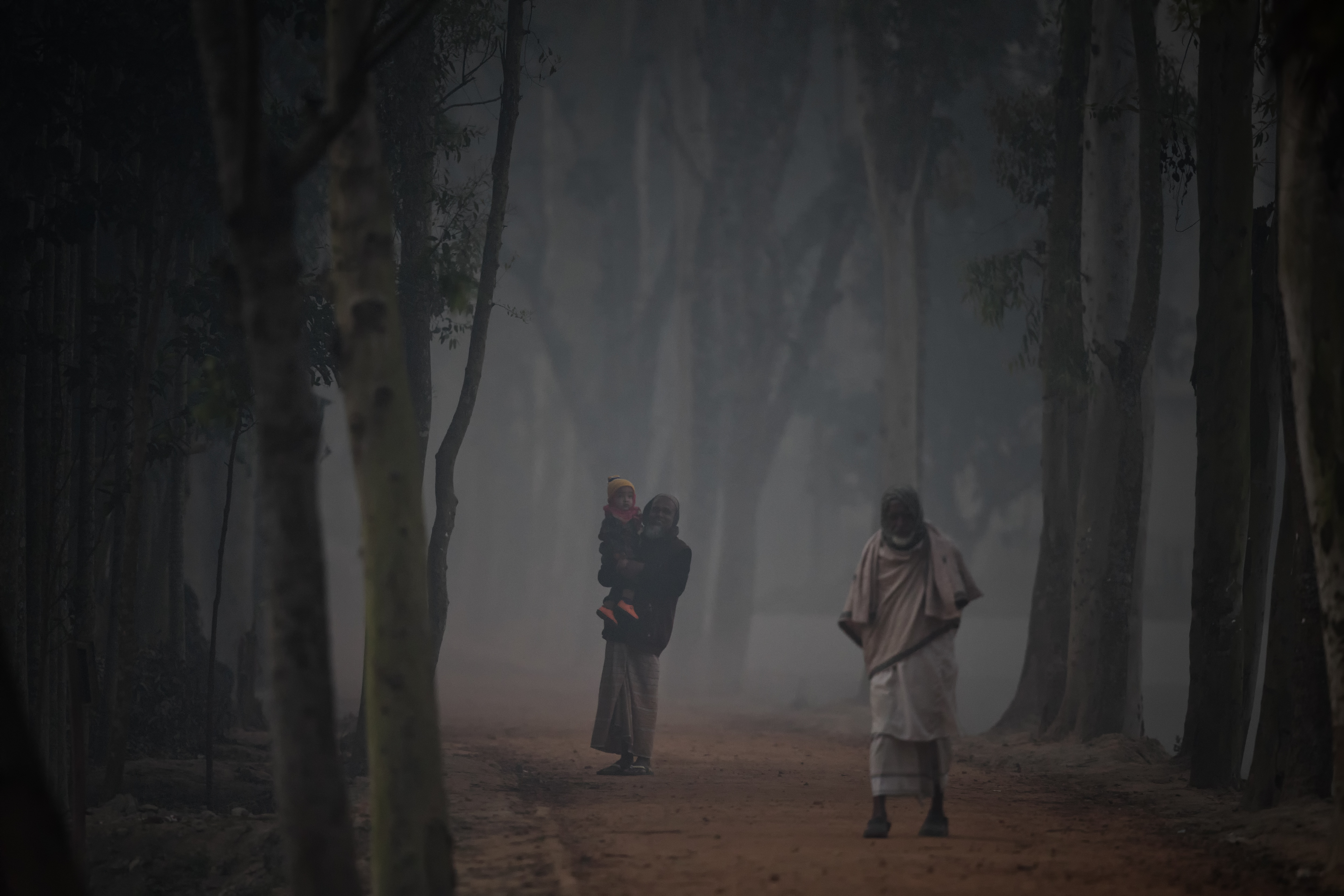 Two men walk along a road that is otherwise still under a blanket of wood smoke and dawn mist.