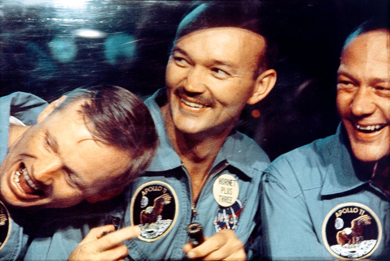 After splashing down safely into the Pacific Ocean, Neil Armstrong, Mike Collins, and Buzz Aldrin smile through the window of the mobile quarantine van.