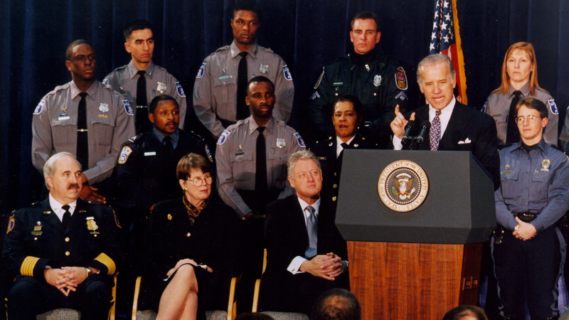 Then-Senator Joe Biden speaks at the signing of the Violent Crime Control and Law Enforcement Act of 1994, as Attorney General Janet Reno, President Bill Clinton, and local law enforcement officials look on.