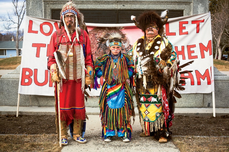 Catcher Cuts the Rope and his son Conan Cuts the Rope, from the Ford Belknap Indian Reservation, and a bear dancer from the Confederated Salish & Kootenai Tribes protesting the bison slaughter at the state capitol in Helena, Montana. The banner behind them reads “Love the Buffalo, Let Them Roam.”