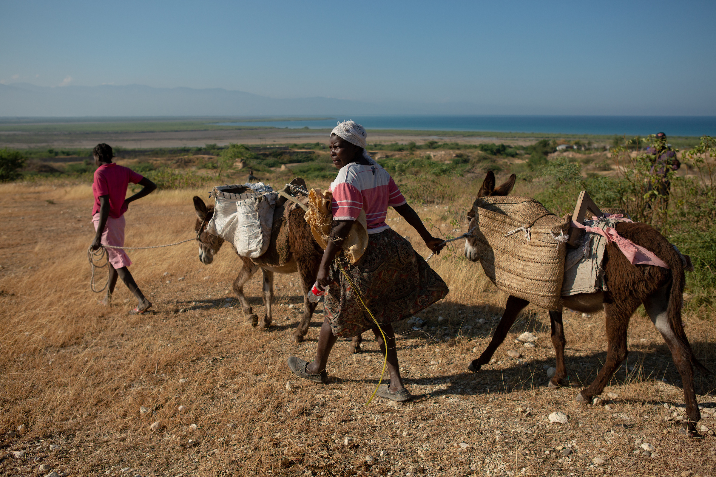 Women walk with their donkeys outside the St. Christophe memorial, the mass gravesite where tens of thousands of earthquake victims are buried, on the ninth anniversary of the 2010 earthquake, just north of Port-au-Prince, Haiti, January 12th, 2019. The property is surrounded on three sides by greater Canaan.