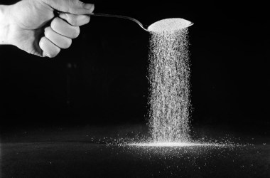 Photo of a person's hand, holding a spoonful of sugar