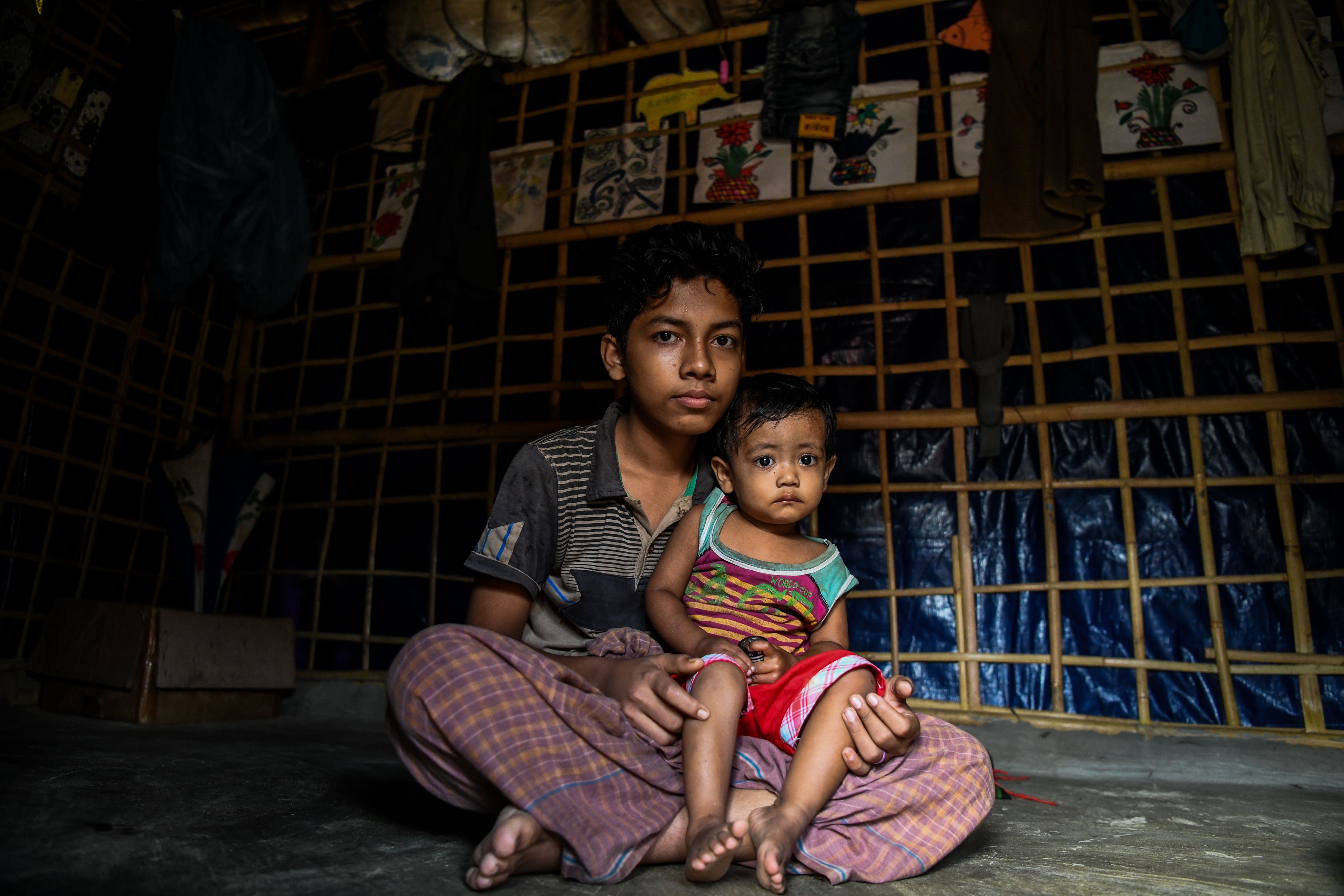 Rohingya refugee boy Kamal Sadiq, 14, holds his cousin, Ruma Sadiq, inside his home at the Kutupalong camp in Ukhia on August 13th, 2018.