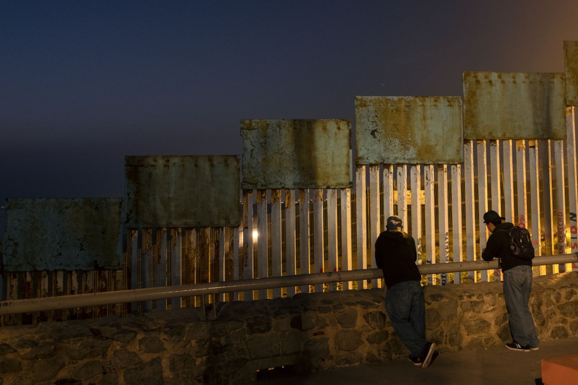 Two migrants lean against a rail next to the U.S.-Mexico border fence in Tijuana, Mexico, on August 10th, 2018.