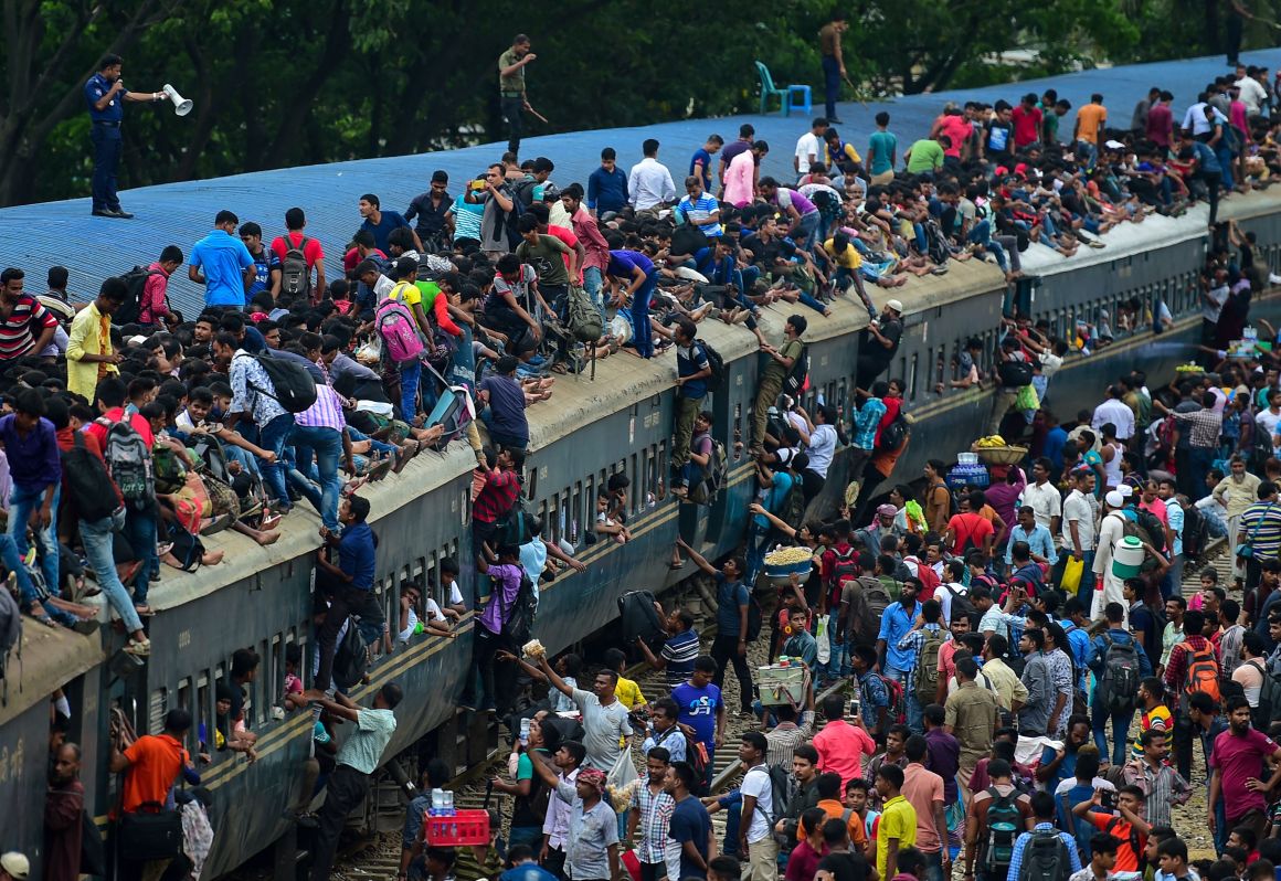 People scramble to reach the roof of an overcrowded train at a station in Dhaka, Bangladesh, on August 20th, 2018. Crowds rushed home from the capital city to be with friends and family during the annual holiday of Eid al-Adha, also known as the Festival of Sacrifice, celebrated by Muslims worldwide.