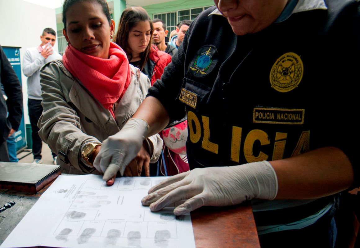 A policeman takes fingerprints of a Venezuelan migrant as a group of migrants wait to apply for resident visas or temporary stay permits at an Interpol facility in Lima, Peru, on August 29th, 2018. Last Friday, Peru enacted rules that mandated that Venezuelans coming into the country show a passport (previously, the law only required an identification card). Since then, hundreds of Venezuelans have applied for asylum in Peru. As Venezuela suffers an unprecedented economic and humanitarian crisis, hundreds of thousands of Venezuelans have fled into other South American countries, escaping intolerable food and medicine shortages in their home country.