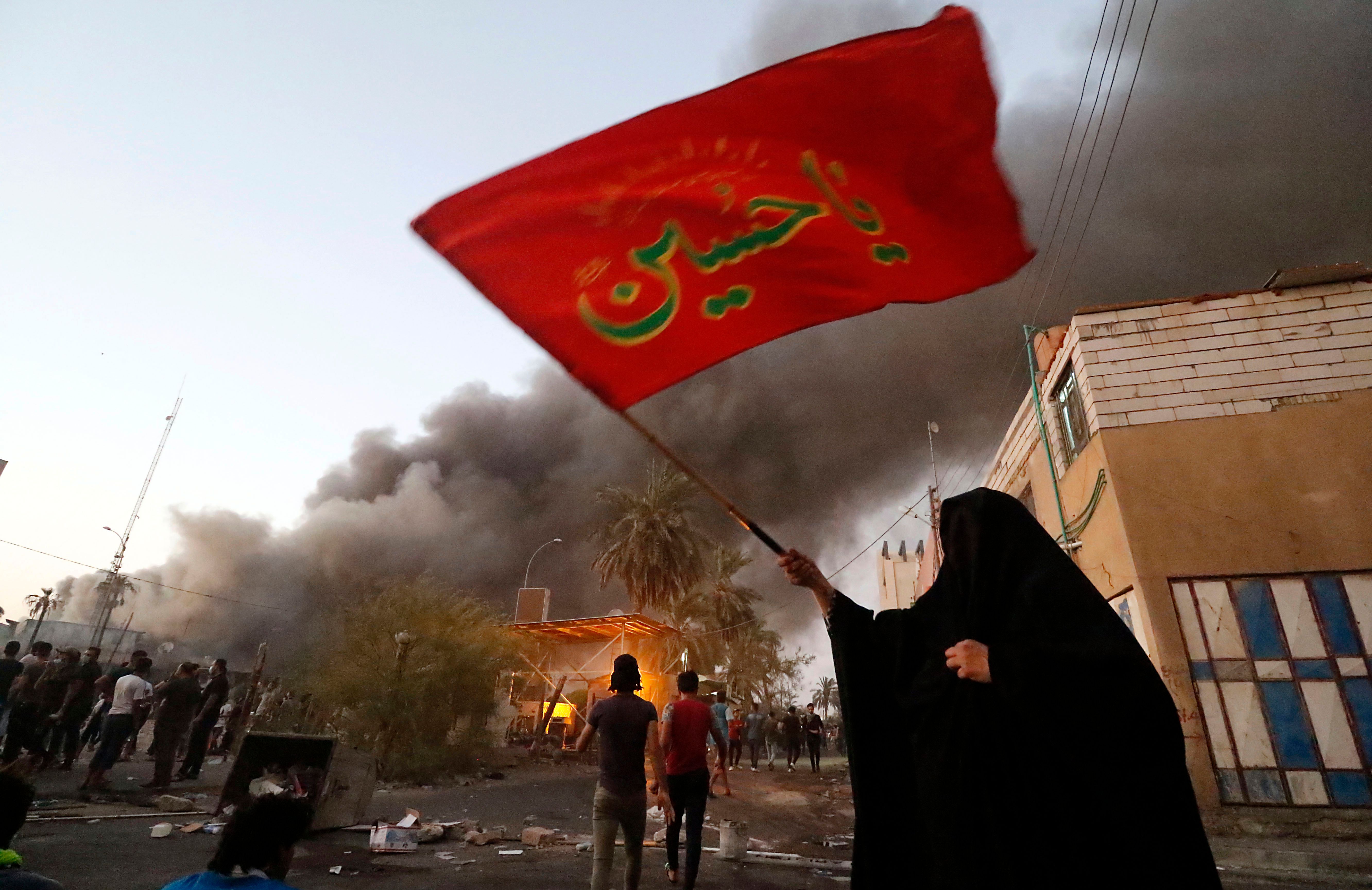 Iraqi protesters break into an official building as one protester waves a regional flag.