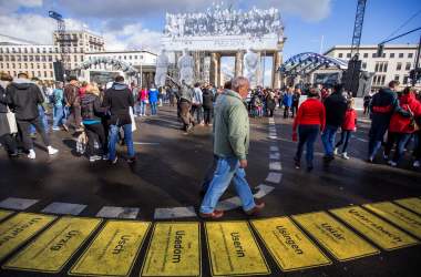 People walk in front of the Brandenburg Gate, decorated with a photo collage by the French street artist and photographer known as JR for German Unity Day, on October 3rd, 2018, in Berlin, Germany. The national holiday celebrates the reunification of East and West Germany in 1990.