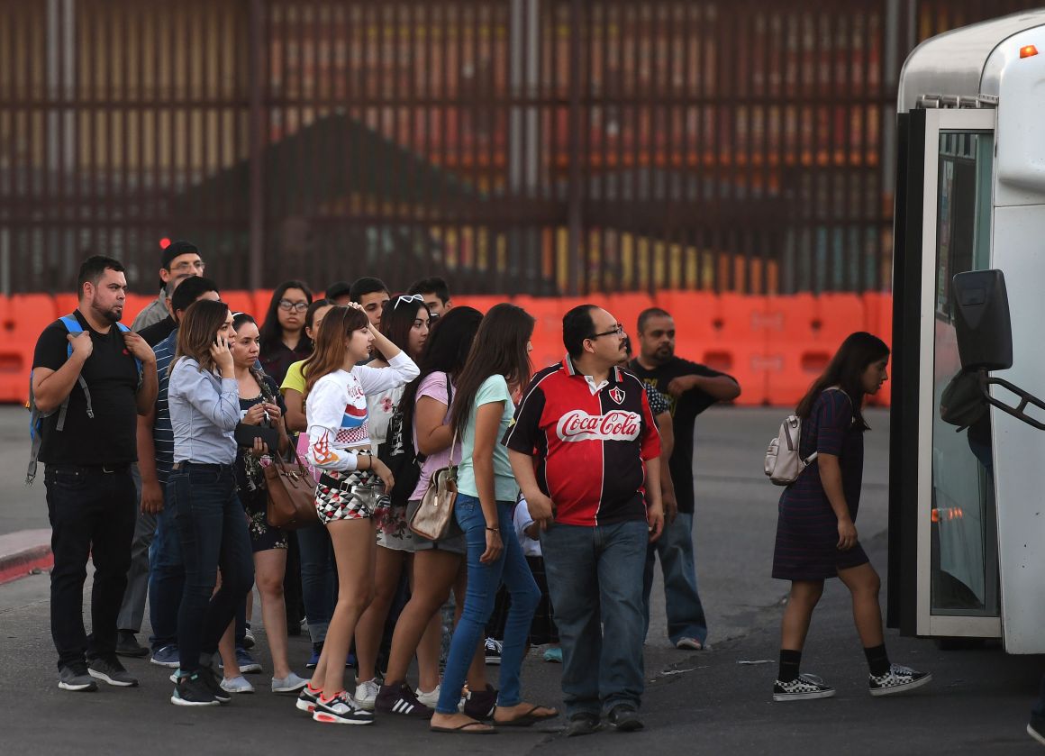 People wait to board a bus for Mexico beside the border wall at the U.S.–Mexico border checkpoint in Calexico, California, on October 25th, 2018.