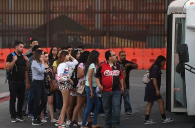 People wait to board a bus for Mexico beside the border wall at the U.S.–Mexico border checkpoint in Calexico, California, on October 25th, 2018.