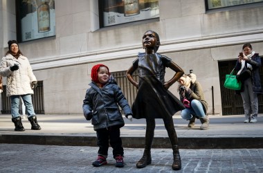 A child stands alongside the Fearless Girl after a ceremony unveiling the statue's new permanent location outside the New York Stock Exchange on December 10th, 2018. The bronze statue, symbolizing female empowerment, has been moved from its Wall Street home opposite the Charging Bull statue in New York City.