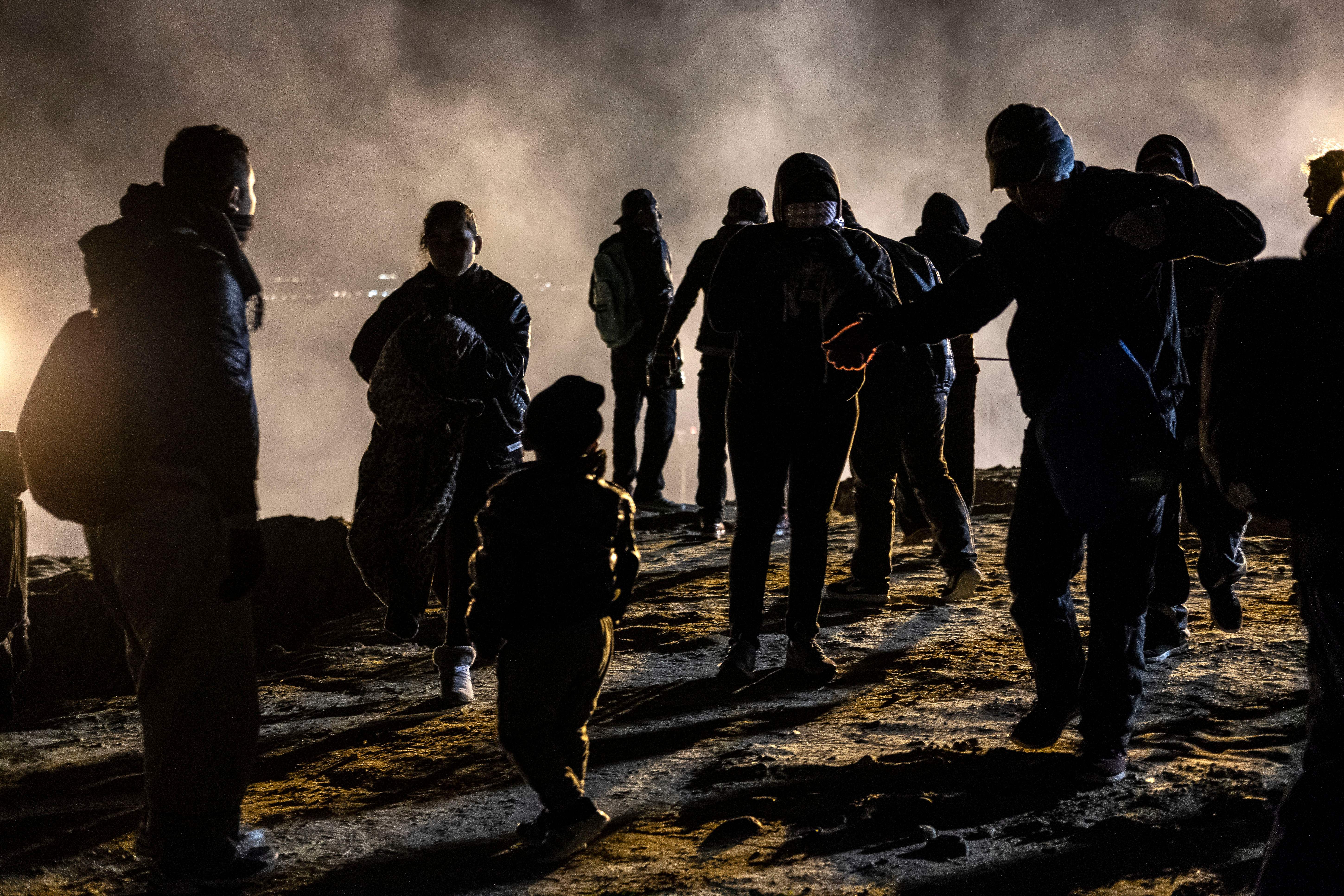 A group of Central American migrants walk away from tear gas thrown by the US border patrol, after they tried to cross from Tijuana to San Diego in the US, as seen from Tijuana, Baja California state, Mexico on January 1, 2019. - Around 100 Central American migrants made a failed attempt on New Year's Eve to cross over from Mexico into the United States. As night fell and people on both sides of the frontier prepared to celebrate New Year's Eve, the migrants tried to cross over but at least two smoke bombs were hurled and they ultimately held back.