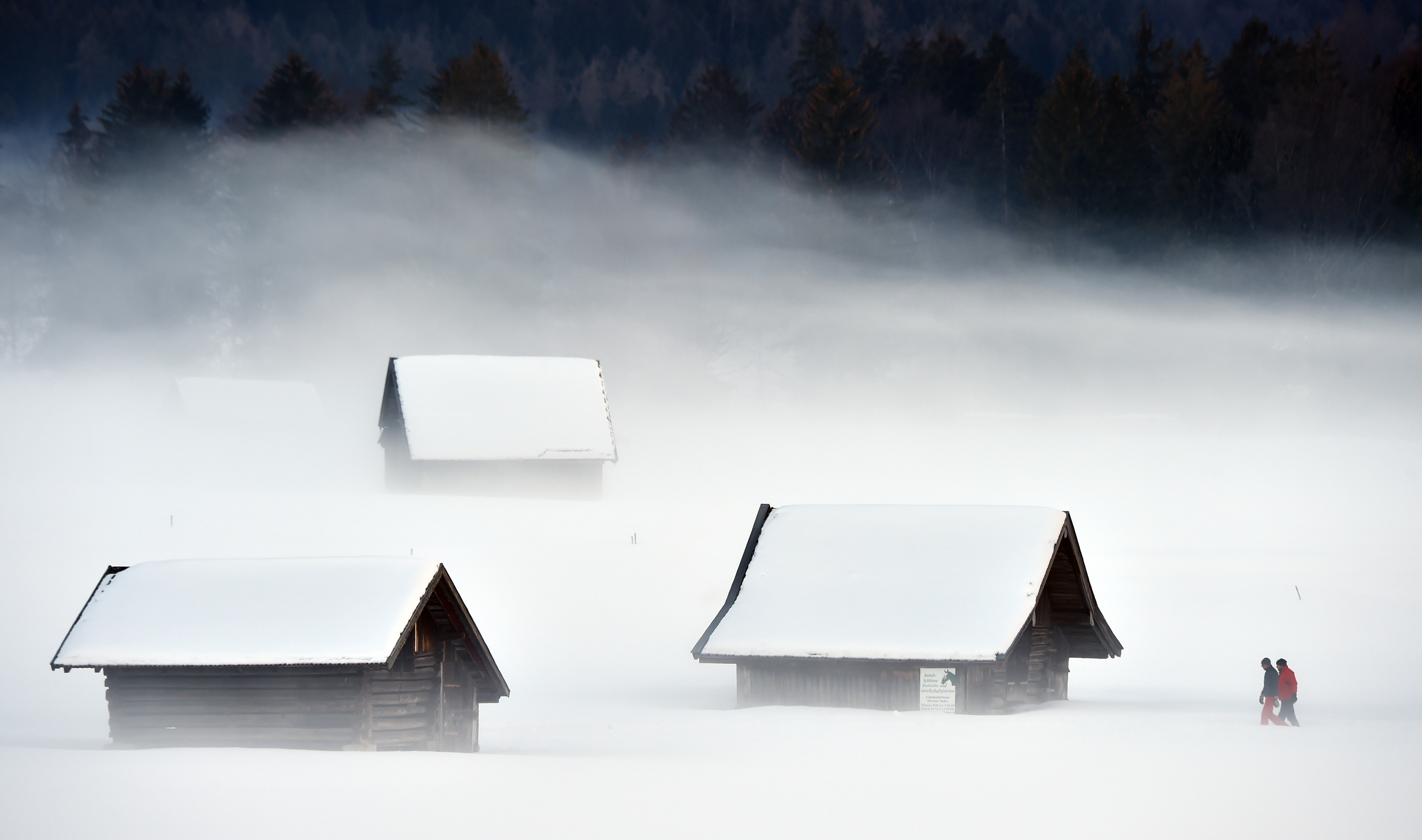 Pedestrian pass a snowy meadow way during foggy winter weather with temperatures by the freezing point in Garmisch-Partenkirchen, southern Germany, on January 27th, 2019.