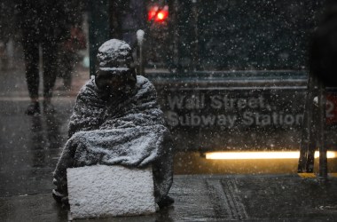 A homeless man sits in the falling snow in the Financial District on January 30th, 2019, in New York City.