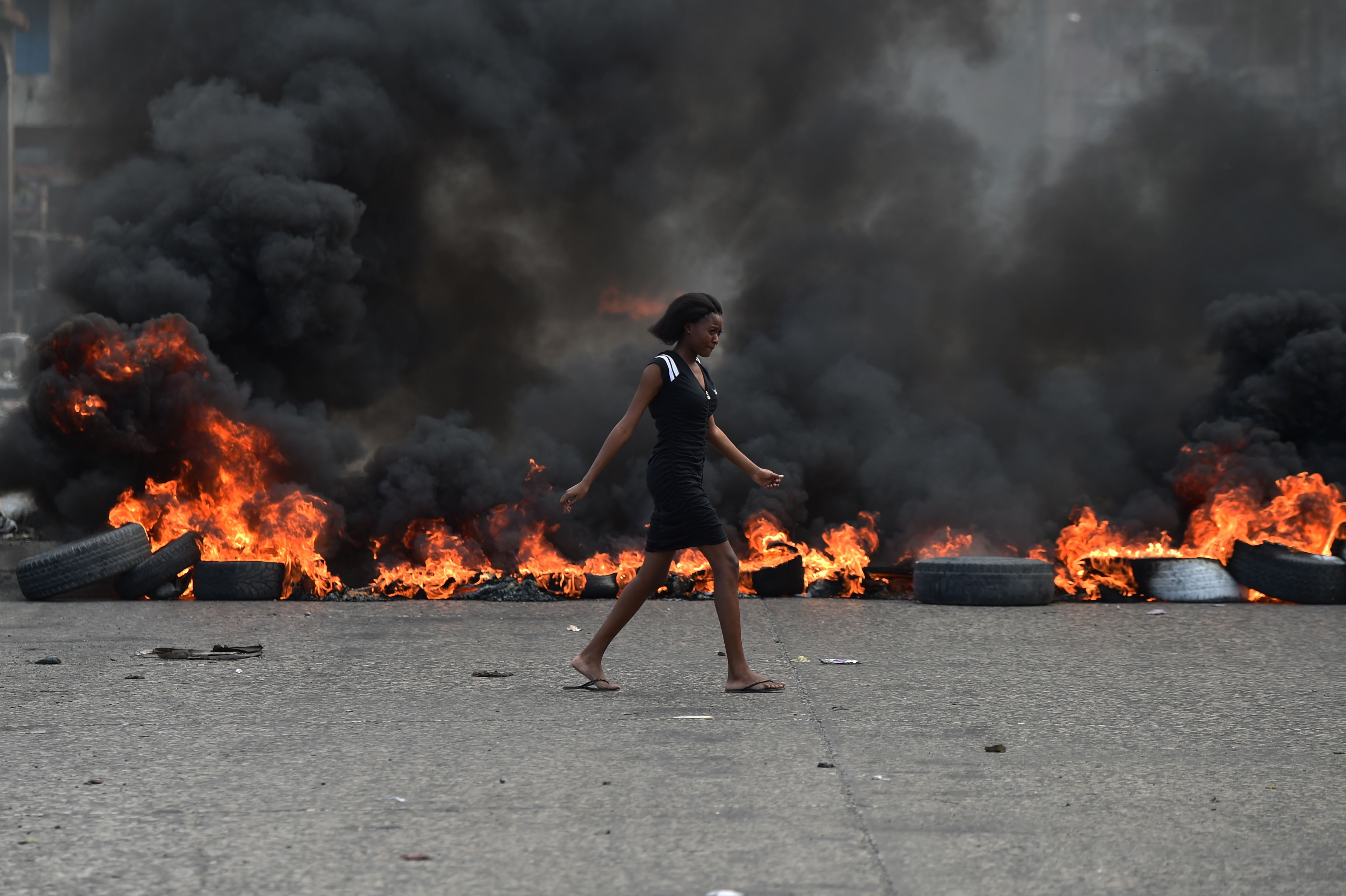 A woman walks past tire barricades set ablaze by demonstrators on February 10th, 2019, the fourth day of protests in Port-au-Prince.