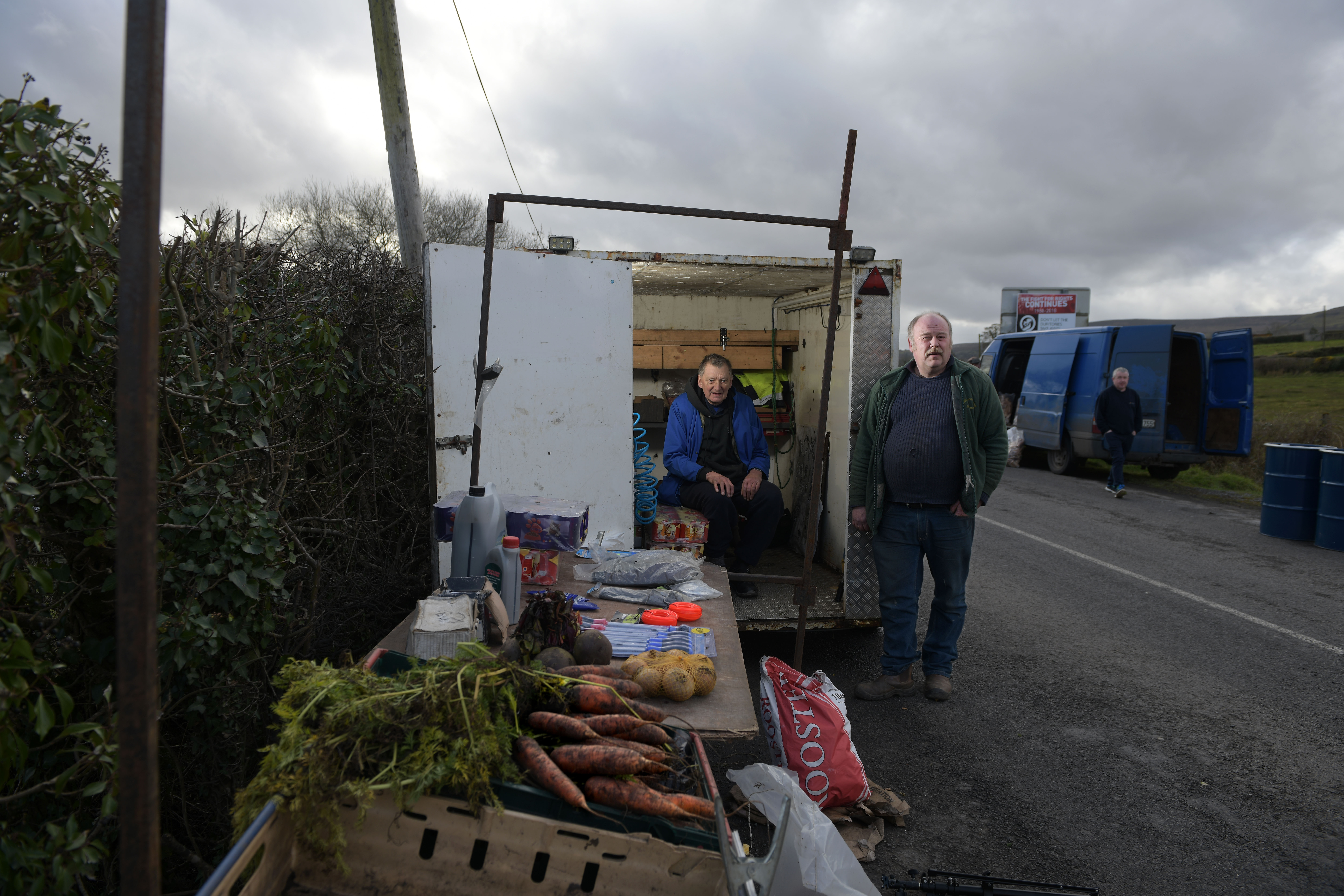 Denny Johnston (right) poses for a photograph alongside John Taylor (left) as he trades from the back of his trailer on the Irish border at the Mullan roadside market on February 17th, 2019, in Mullan, Northern Ireland. Johnston, who buys and sells his goods on both sides of the border, fears for his business if a hard border returns.