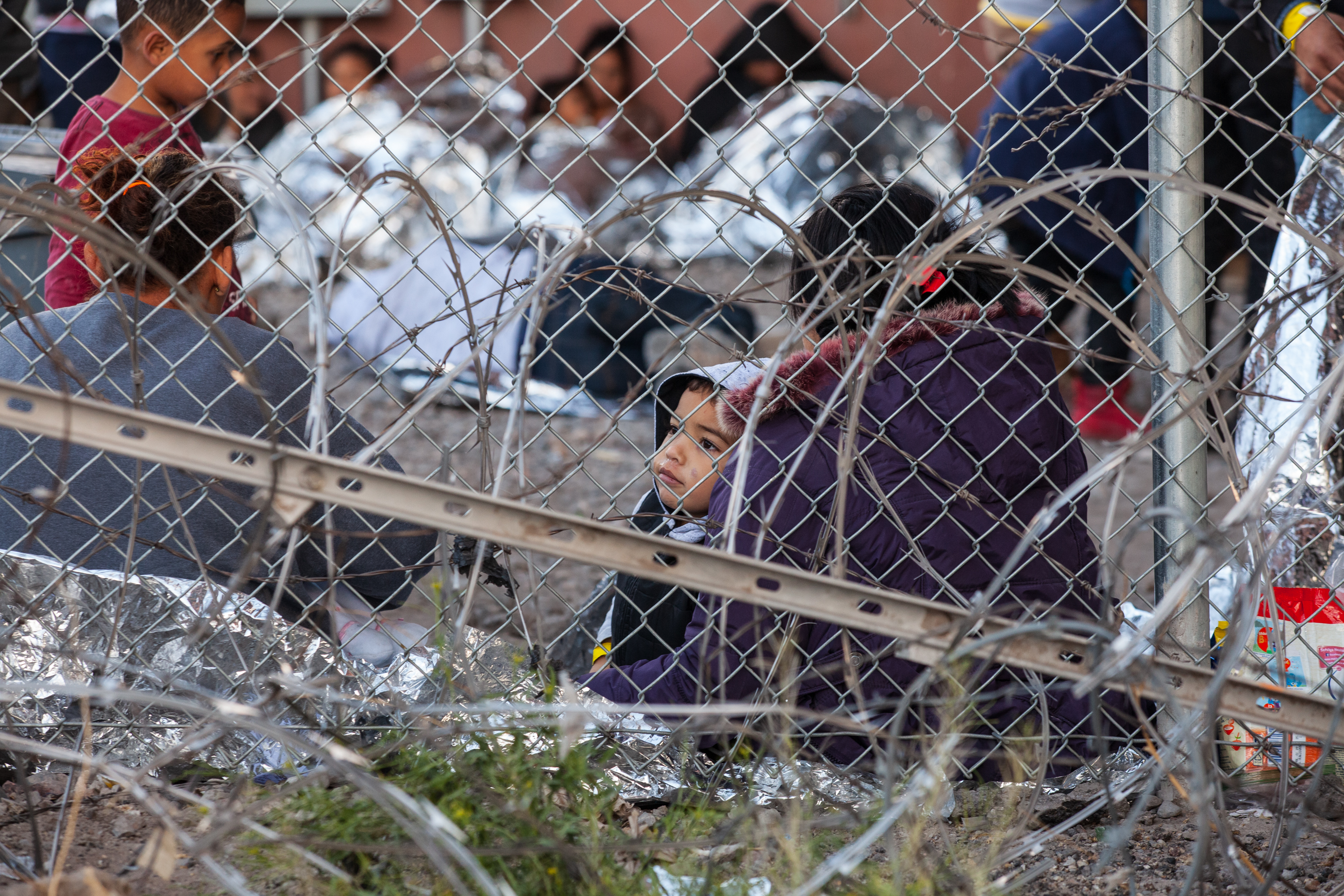 A child sits behind military-style concertina wire and chain link fencing as CBP holds him and his family with hundreds of other in the enclosure on March 28th.