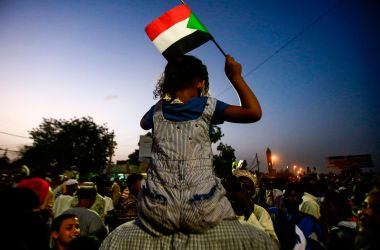 A Sudanese child waves a national flag as she sits atop the shoulders of a man during a late demonstration outside the army headquarters in the Sudanese capital Khartoum on April 12th, 2019. Protesters defied a night-time curfew to keep up four months of mass demonstrations.