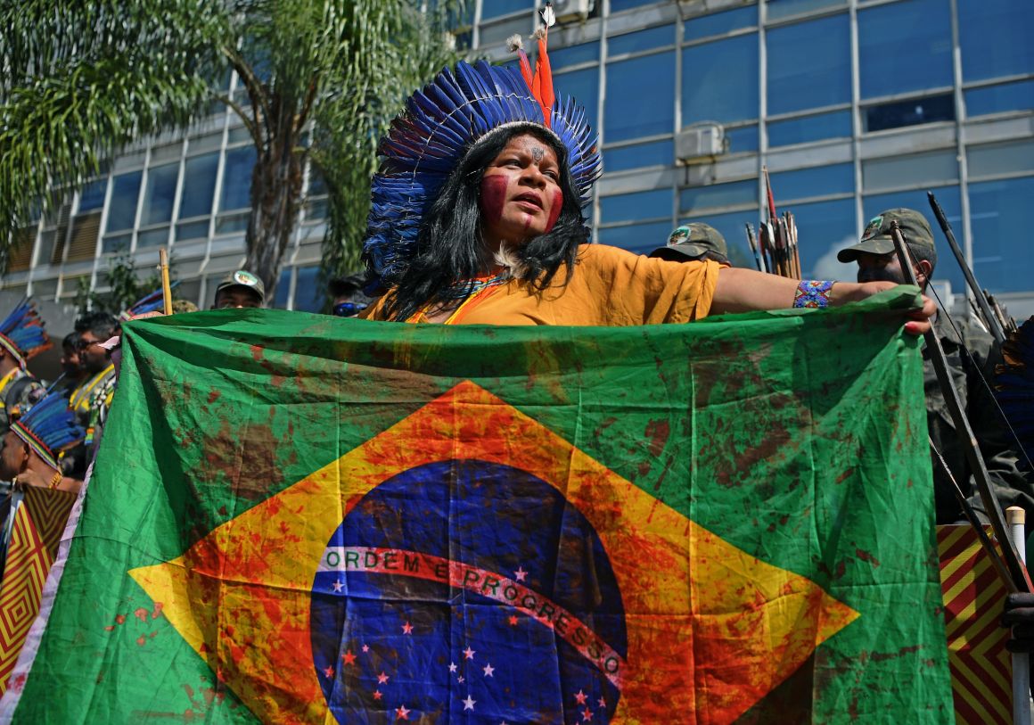 An Indigenous woman holds a Brazilian national flag stained in with a blood-like red during a march in Brasilia on April 26th, 2019, on the last day of a protest to defend Indigenous land and rights.