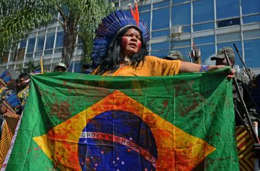 An Indigenous woman holds a Brazilian national flag stained in with a blood-like red during a march in Brasilia on April 26th, 2019, on the last day of a protest to defend Indigenous land and rights.