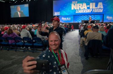 Skippy Thomas, a member of the National Rifle Association, takes a selfie with President Donald Trump in the background during the NRA's annual meeting at Lucas Oil Stadium in Indianapolis, Indiana, on April 26th, 2019.