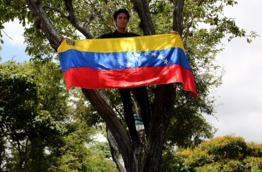 A student standing in a tree displays a Venezuelan flag during a rally in support of opposition leader Juan Guaidó and against Nicolás Maduro at Universidad Central de Venezuela on May 2nd, 2019, in Caracas, Venezuela. After two days of violent clashes between pro-Guaidó and pro-Maduro groups including civilian, police, and military forces that resulted in four dead and over 100 wounded, Venezuelans supporting Guaidó are taking to the streets and responding to the call for strikes.