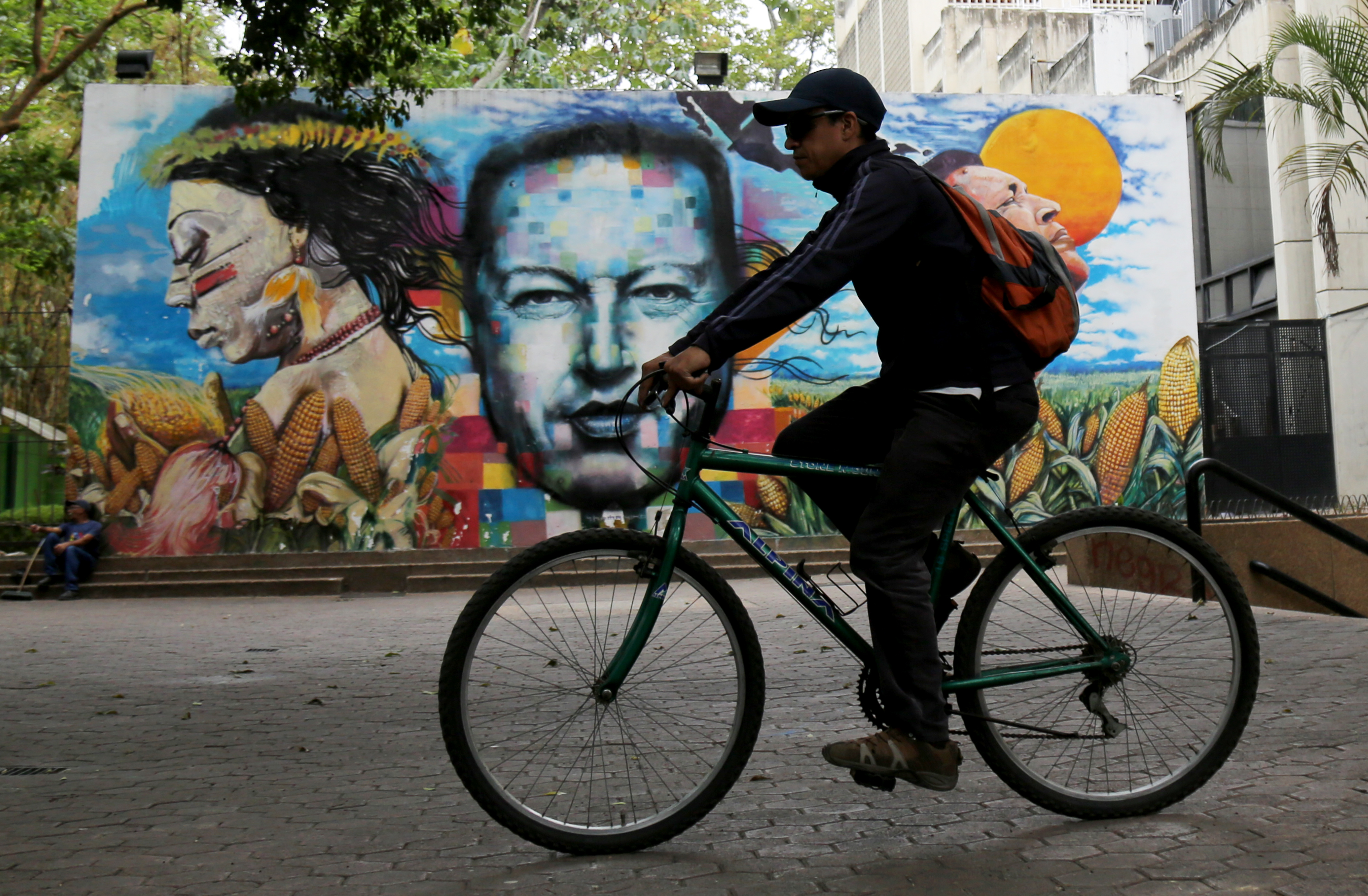 A Venezuelan rides his bike to work in front of a mural of the late President Hugo Chávez near Teresa Carreno Theatre on May 8th, 2019, in Caracas, Venezuela. As the country goes through a political, economic, and social crisis, Venezuelan opposition led by Juan Guaidó, recognized by many more than 50 nations as the country's rightful interim ruler, is still trying to oust Nicolás Maduro after a failed uprising attempt on April 30th.