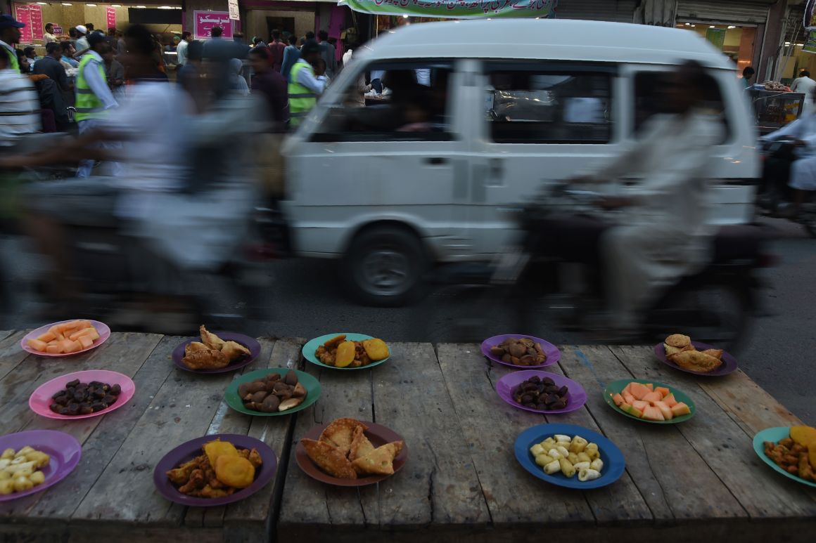 Pakistani commuters ride past plates of Iftar food placed for residents to break their fast along a street in Karachi, Pakistan, on May 9th, 2019.