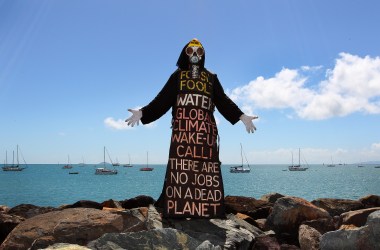 Benny Zable, a performance artist for peace and environment, stands in costume at the edge of Airlie Bay during an anti-Adani Carmichael coal mine rally on April 26th, 2019, in Airlie Beach, Australia.