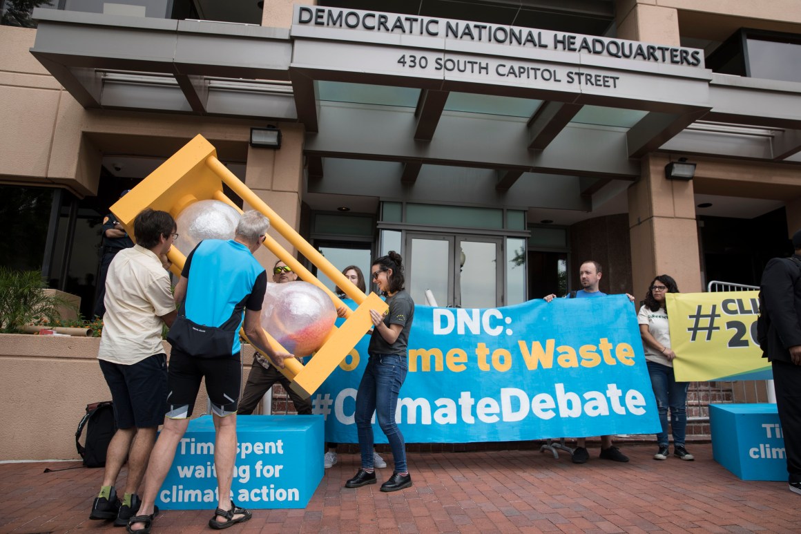 A group of people flip over an hourglass in front of the Democratic National Committee headquarters during a Green Peace rally to call for a presidential climate debate on June 12th, 2019, in Washington, D.C.