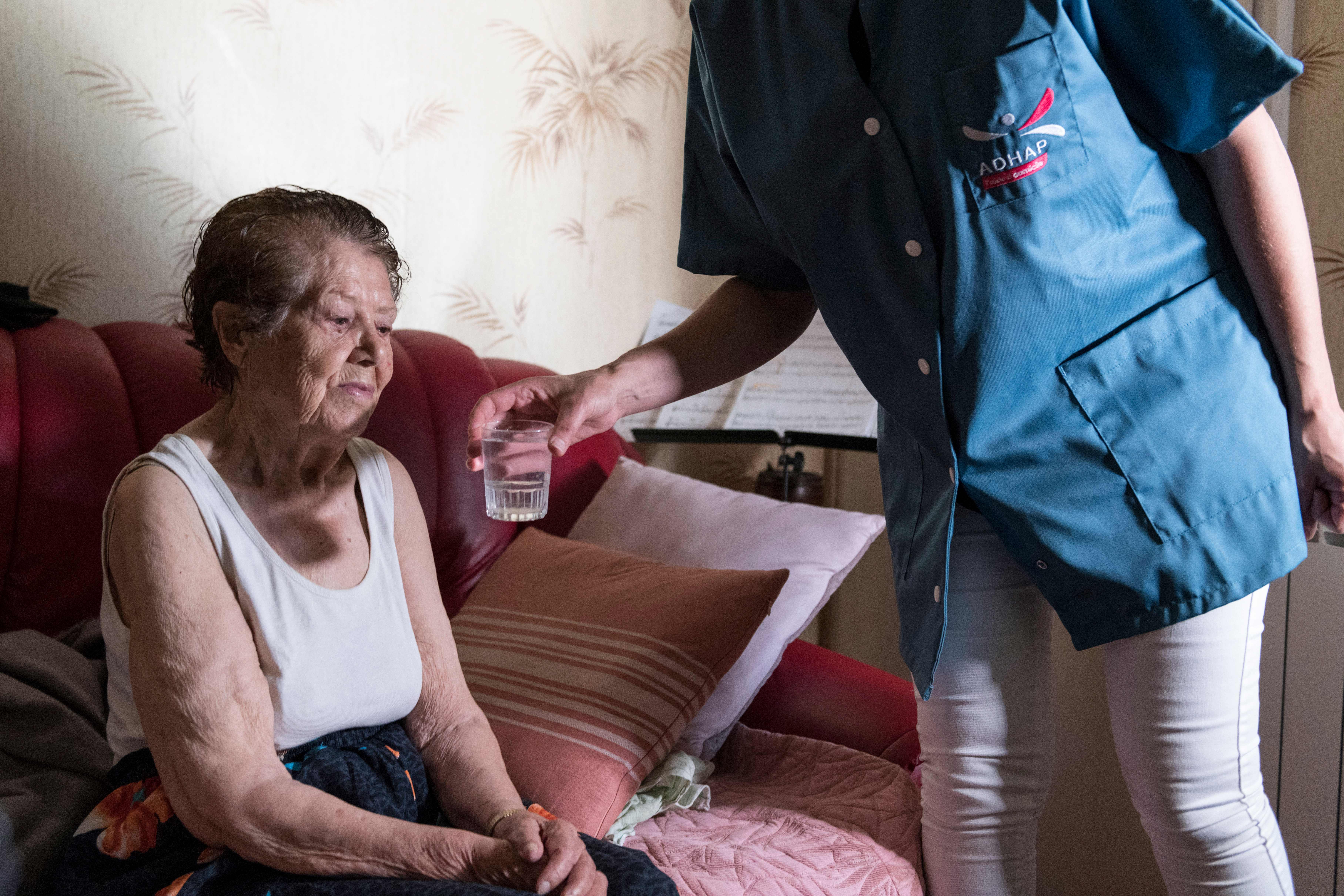 A personal care assistant gives a glass of water to an elderly person as she visits her house to help her to avoid heatstroke and dehydration during the heat wave on June 25th, 2019, in Clermont-Ferrand, France.