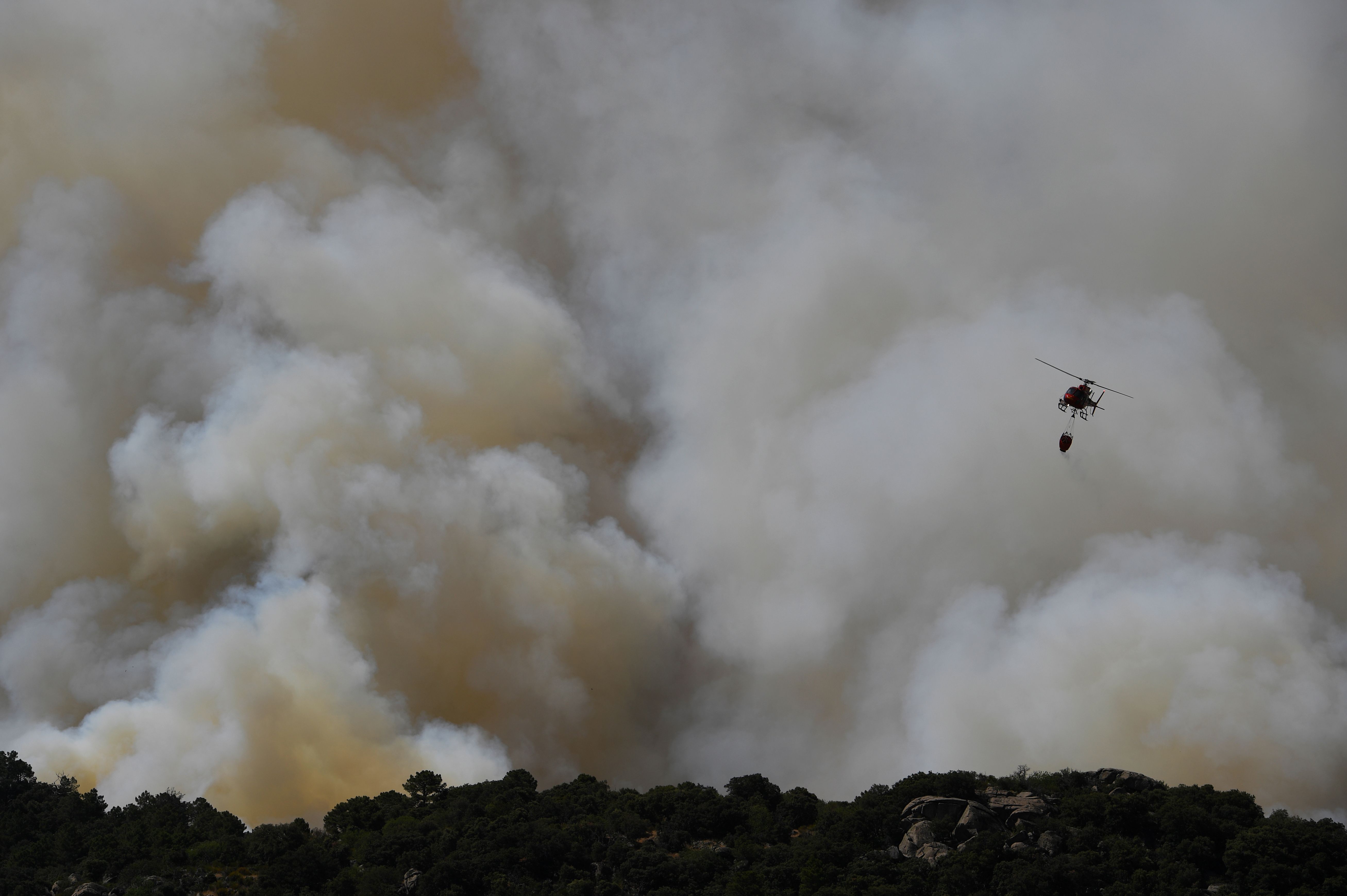 A helicopter drops water over a wildfire in the outskirts of Cenicientos in central Spain on June 29th, 2019. Spain was hit by more wildfires as temperatures remained sky-high in the Europe-wide heat wave, authorities said, just as firefighters finally managed to contain another blaze they had been tackling for nearly 72 hours.