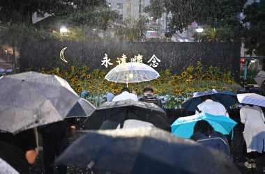 People bow to pay their respects after leaving sunflowers on a stage, as they attend a memorial event during heavy rainfall in Hong Kong on July 11th, 2019.