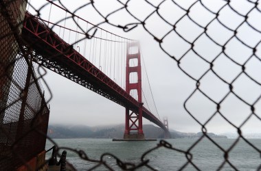 A view of the Golden Gate Bridge is seen through a hole in a fence closing off a part of Fort Point in San Francisco.