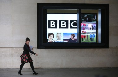 A woman walks past a bank of television screens displaying BBC channels in the BBC headquarters on November 12th, 2012, in London, England.