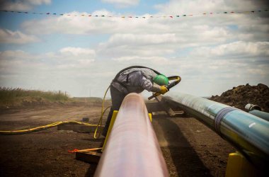 A construction worker specializing in pipe-laying sandblasts a section of pipeline on July 25th, 2013, outside Watford City, North Dakota.