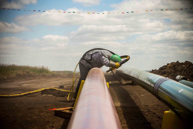 A construction worker specializing in pipe-laying sandblasts a section of pipeline on July 25th, 2013, outside Watford City, North Dakota.