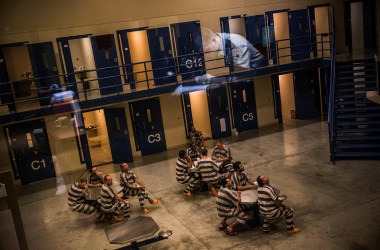 An officer is reflected in the glass as inmates sit in the county jail on July 26th, 2013, in Williston, North Dakota.